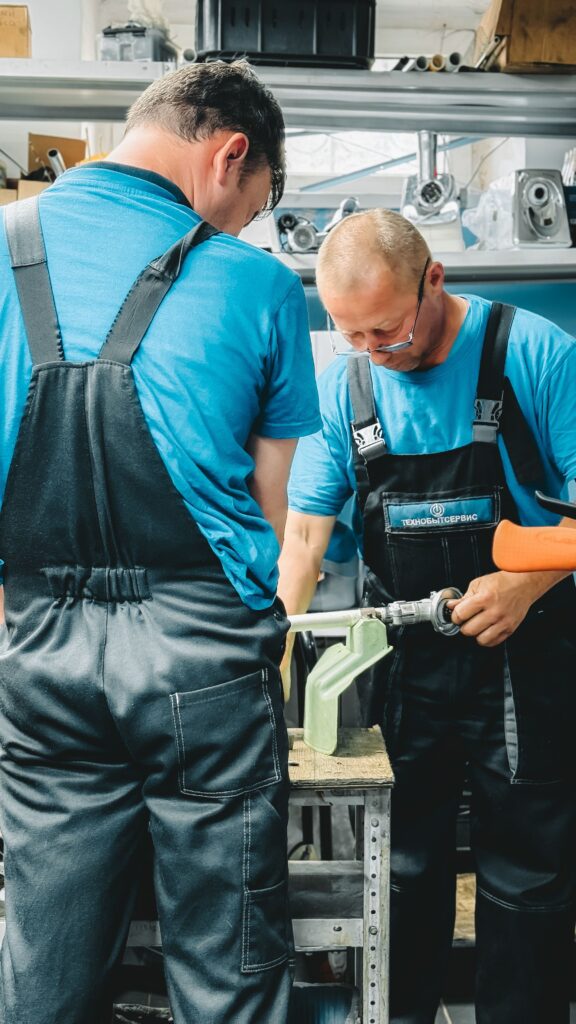 pexels-photo-32588546-32588546 Two male technicians work together using tools in a busy workshop.