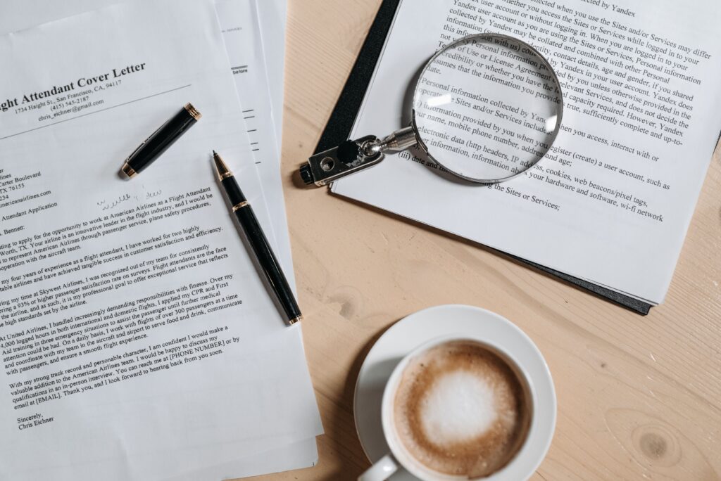 pexels-photo-8112194-8112194-1 A top view of coffee and job application documents with a magnifying glass on a wooden desk.